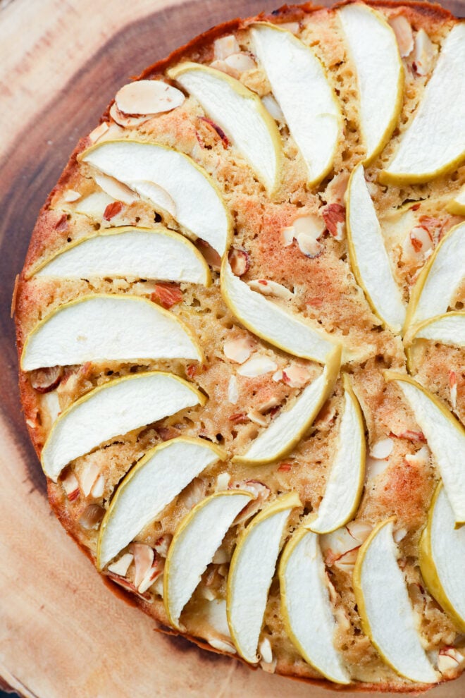 A round cake topped with a decorative pattern of thinly sliced apples and scattered almond slivers.
