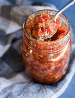 A spoon scoops chunky bacon onion jam from a glass mason jar.