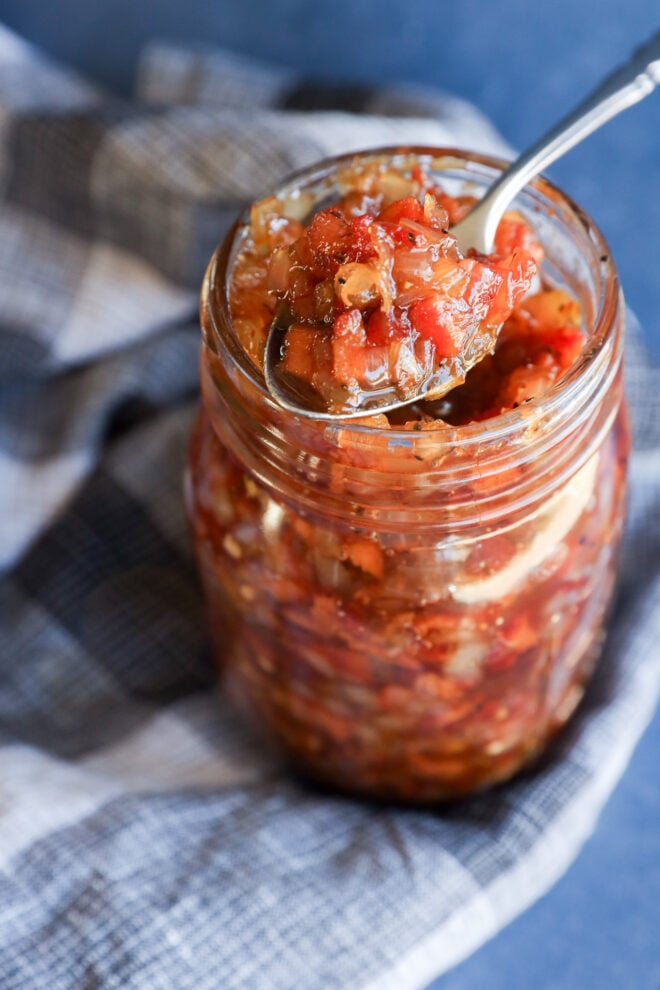 A spoon scoops chunky bacon onion jam from a glass mason jar.