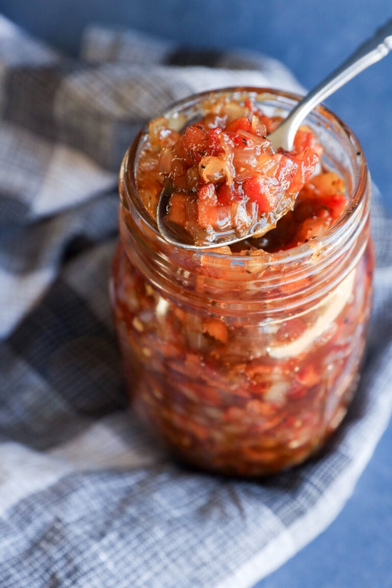 A spoon scoops chunky bacon onion jam from a glass mason jar.