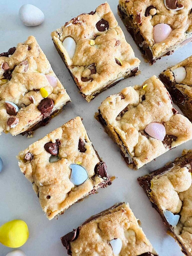 Square slices of cookie bar filled with chocolate chips and pastel-colored candy-coated chocolates.