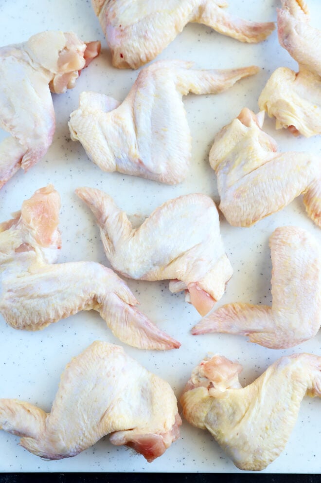 Several raw chicken wings arranged on a white surface.