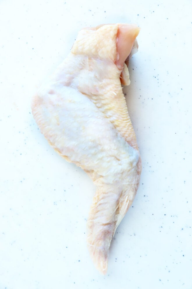 Raw chicken wing on a white speckled surface.