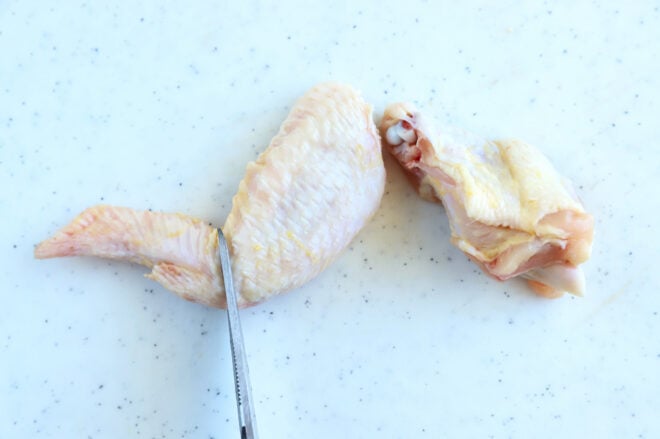 A knife cutting through a raw chicken wing on a cutting board.