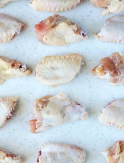 Raw chicken wings arranged in a grid on a white cutting board.