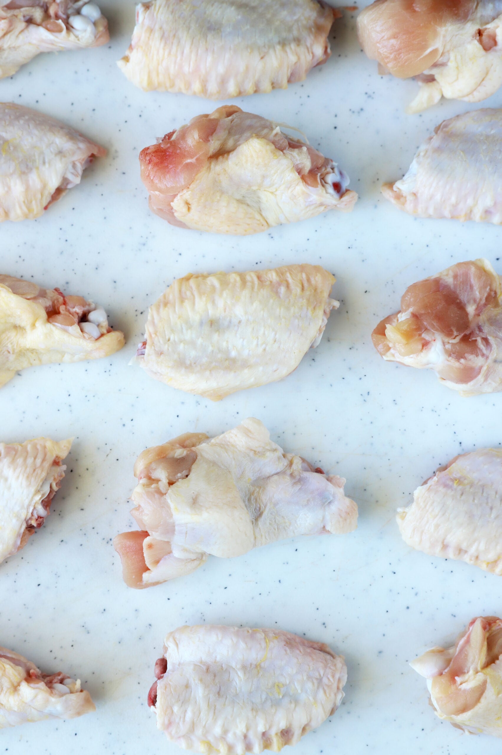 Raw chicken wings arranged in a grid on a white cutting board.