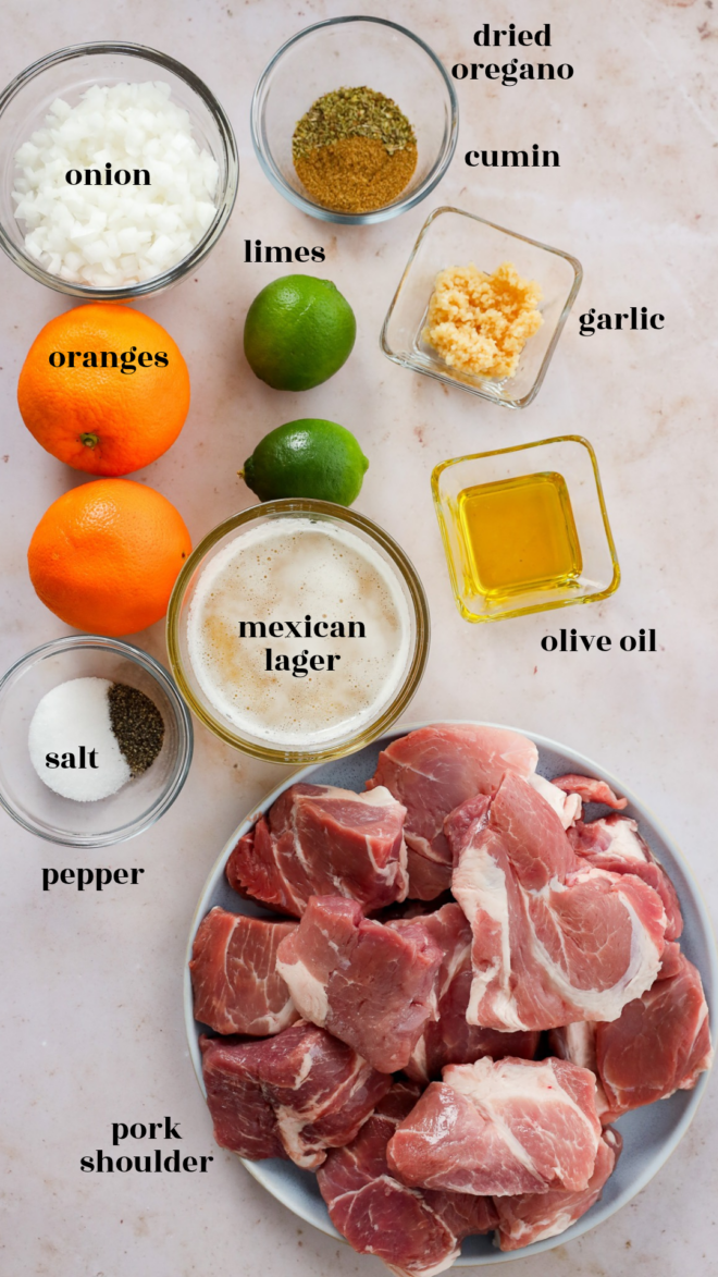 Top-down view of instant pot carnitas ingredients including pork shoulder, Mexican lager, oranges, limes, onion, garlic, olive oil, dried oregano, cumin, salt, and pepper, each labeled with its name.