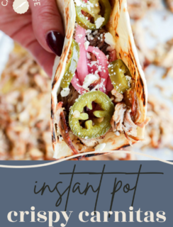 A hand holds an instant pot crispy carnitas taco topped with pickled red onions, sliced jalapeños, and crumbled cheese.