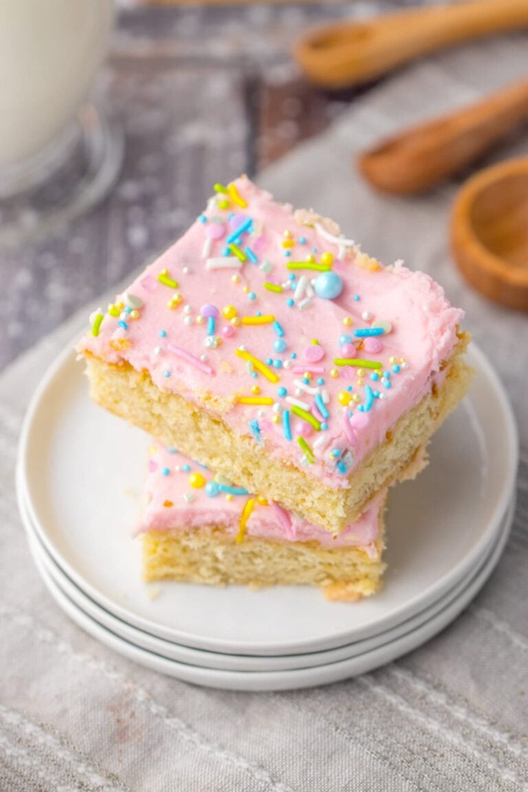 Two stacked sugar cookie bars with pink frosting and colorful sprinkles on a small white plate.