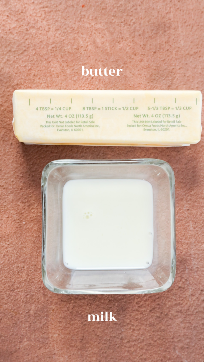 A stick of butter labeled with measurements above a small glass bowl of milk.