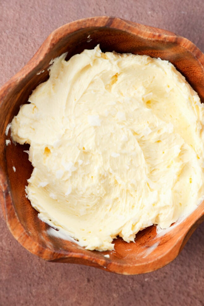 A wooden bowl filled with swirled butter topped with flakes of sea salt.